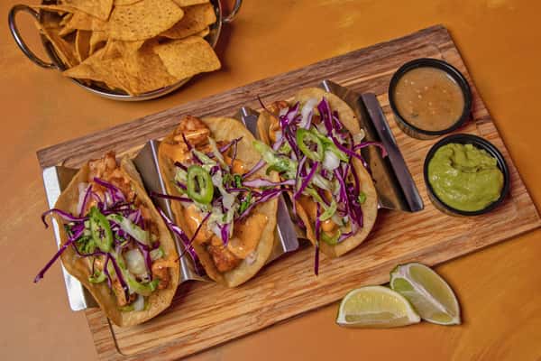 Tacos arranged on a wooden board with lime wedges