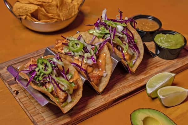 Tacos with slaw and avocado arranged on a wooden board
