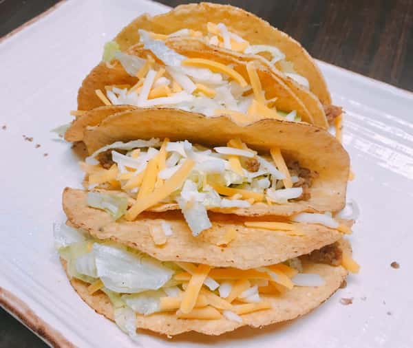 four hard shell tacos with cheese and lettuce