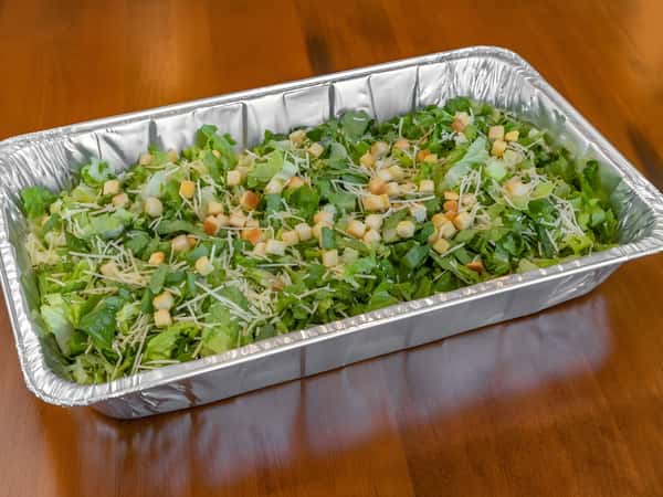 Large catering tray of fresh chopped salad topped with cheese, vegetables, and croutons.