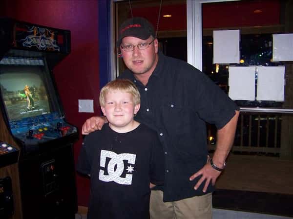 a father and son posing next to an arcade machine