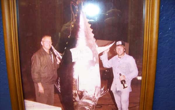 a framed photo of two men posing next to a large tuna