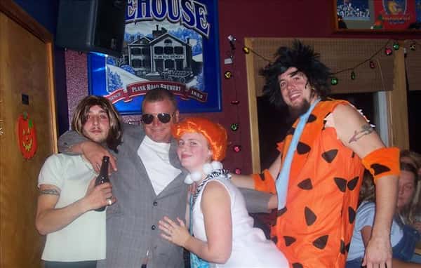 four friends posing, two are dressed as the Flinstones