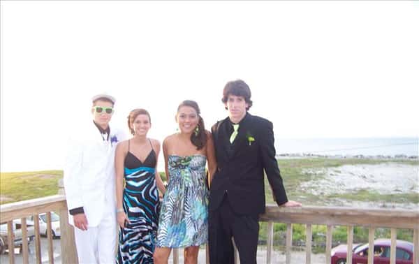 a small group of highschool-aged kids in suits and prom dresses, posing by the beach