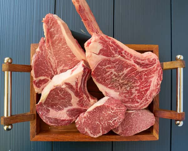 Raw bone in steaks arranged upright on a wooden rack against a blue background.