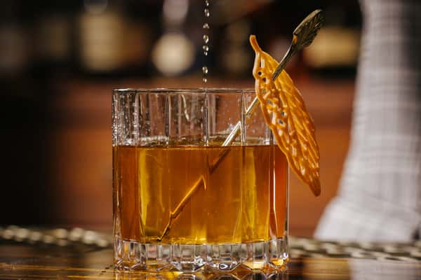 Old fashioned cocktail in a rocks glass with a large ice cube and a citrus peel garnish.