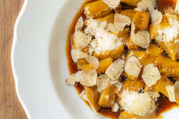 Pasta dish topped with shaved cheese and sauce on a white plate.