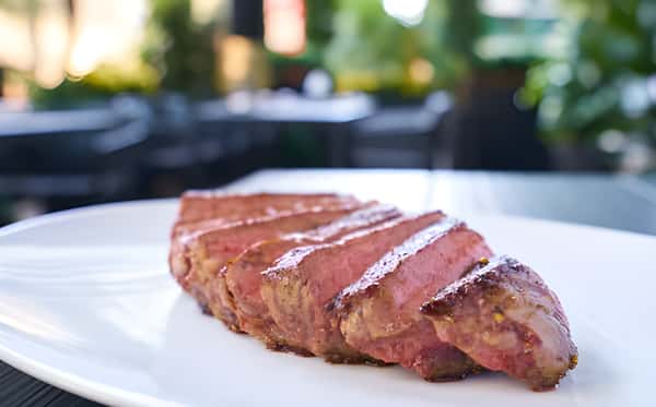 Sliced steak arranged on a white plate with a blurred outdoor background.