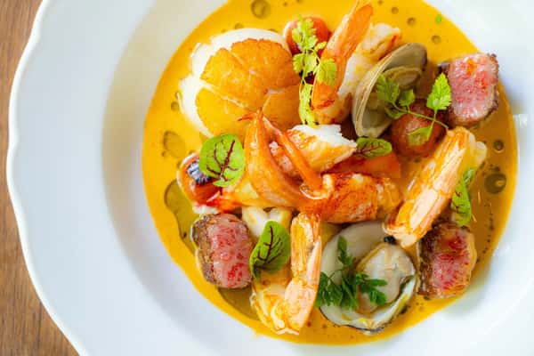 Plated seafood dish with shrimp and garnishes in a yellow sauce.