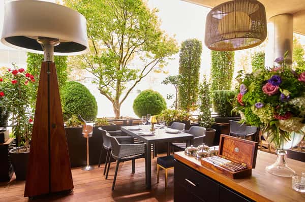 Outdoor patio seating with tables, chairs, and umbrellas surrounded by greenery.