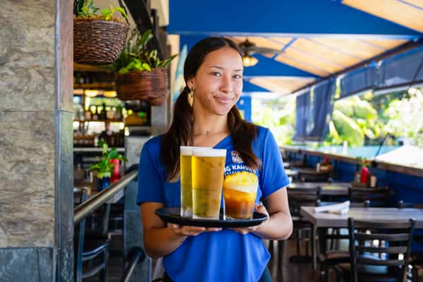 restaurant server holding two cold beers on a tray in a lively outdoor dining setting