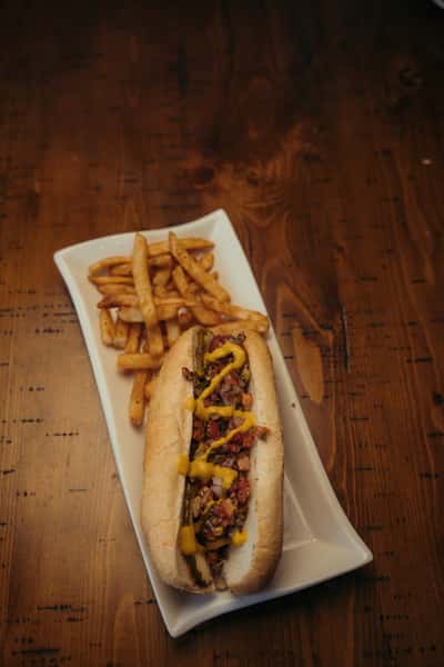 Grilled sausage hoagie topped with diced onions, tomatoes, and mustard, served with crispy seasoned fries on the side.
