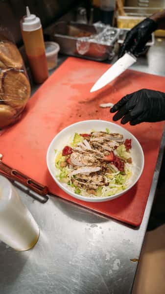 Freshly prepared grilled chicken salad with mixed greens, sliced strawberries, and walnuts, ready to be served for a healthy meal.