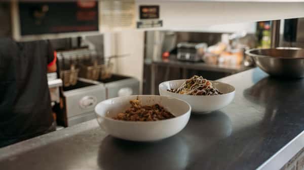 Two freshly prepared bowls of hearty meat and veggie dishes, one topped with creamy sauce, ready to be served from the kitchen line.