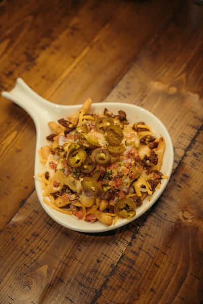 Loaded fries topped with melted cheese, seasoned ground beef, pico de gallo, and sliced jalapeños served in a white skillet-style bowl.