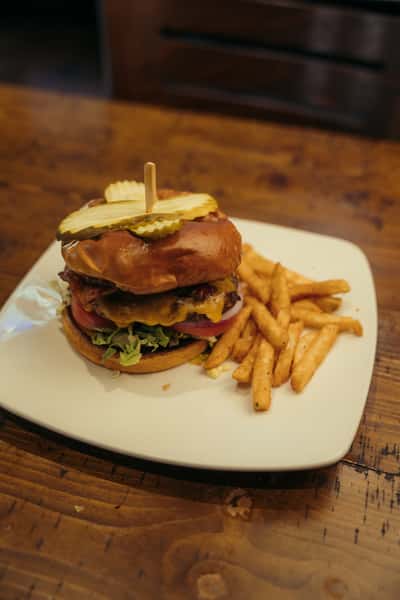Juicy cheeseburger with crispy bacon, pickles, lettuce, tomato, and onions on a toasted bun, served with golden French fries.