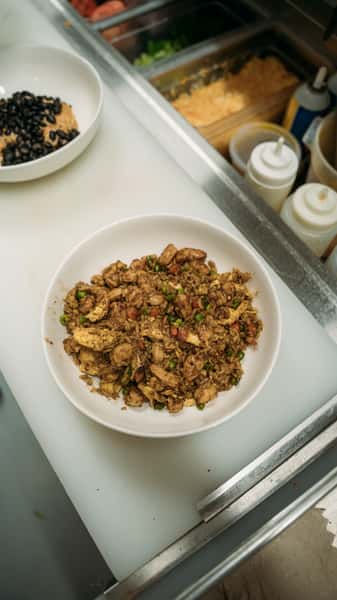 Flavorful bowl of chicken fried rice with tender grilled chicken, peas, and diced vegetables, seasoned to perfection for a hearty and savory meal.
