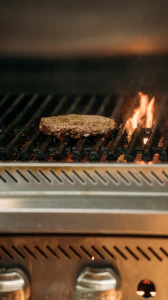 Juicy beef patty sizzling on an open-flame grill, with char marks and flames rising for a smoky, freshly grilled burger.