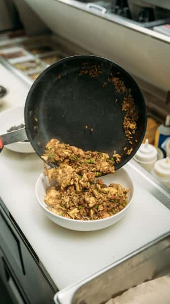 Hot skillet-to-bowl transfer of savory fried rice with chicken, peas, and vegetables, served fresh from the kitchen.
