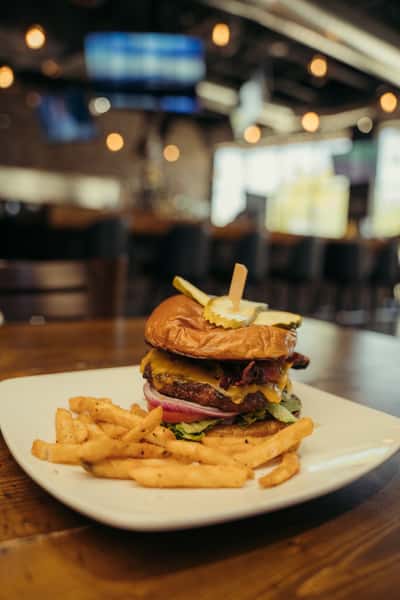 Juicy cheeseburger with crispy bacon, pickles, lettuce, tomato, and onions on a toasted bun, served with golden French fries.