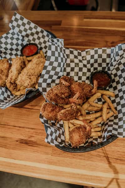 Crispy fried shrimp and golden French fries served in a basket with tangy dipping sauce, perfect for a hearty seafood meal.