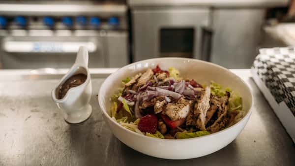 Fresh grilled chicken salad with mixed greens, red onions, strawberries, and walnuts, served with a side of balsamic dressing.
