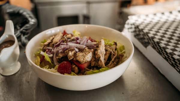 Fresh grilled chicken salad with mixed greens, red onions, strawberries, and walnuts, served with a side of balsamic dressing.
