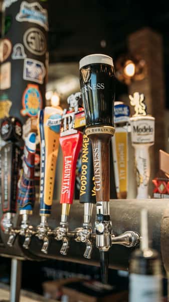 Close-up of beer taps at a bar featuring Guinness, Voodoo Ranger, Lagunitas, Modelo, and other craft beers, perfect for draft beer lovers.