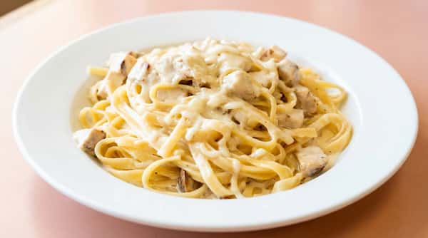 Fettuccine Alfredo with chicken and mushrooms, covered in creamy white sauce on a white plate.