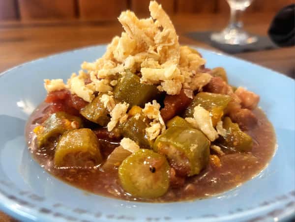 Stewed okra and tomatoes topped with crispy fried onions, served in a light blue bowl.