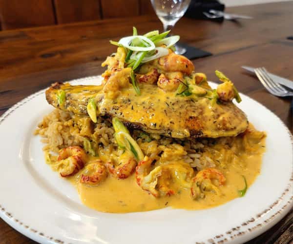 This dish features a blackened fish fillet topped with a creamy crawfish sauce, garnished with sliced green onions, and served over a bed of seasoned rice.