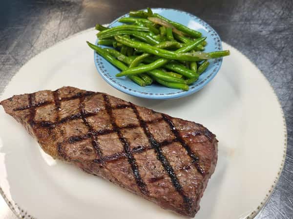 Grilled steak with char marks served alongside sautéed green beans in a small blue bowl.