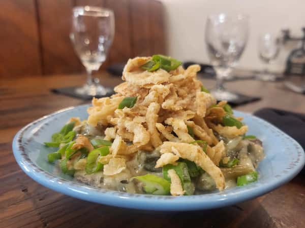 Green bean casserole topped with crispy fried onions and chopped green onions, served in a rustic blue bowl.