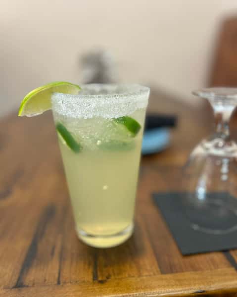 Lime margarita with jalapeño slices in a sugar-rimmed glass, garnished with a lime wedge on a wooden table.