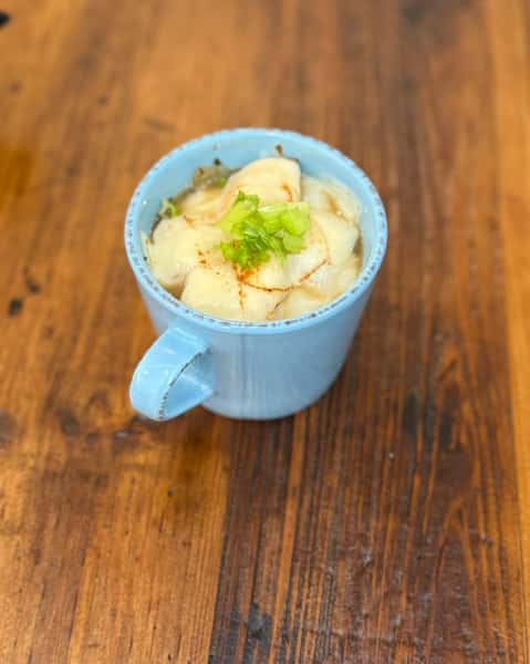 French onion soup in a blue mug topped with melted cheese, toasted bread slices, and garnished with green herbs.