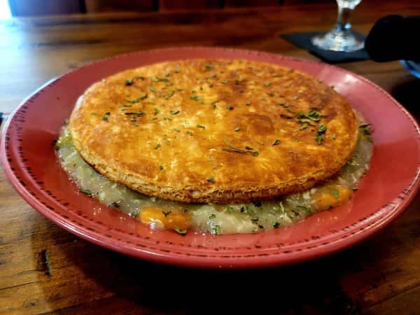 Golden-brown pot pie with a flaky crust, filled with creamy chicken and vegetables, served on a red plate.