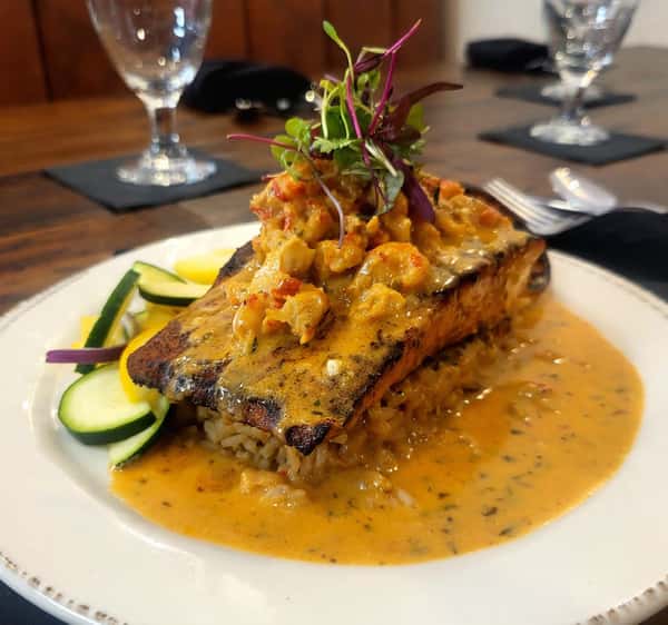 Blackened salmon fillet topped with a rich crawfish cream sauce and microgreens, served over seasoned rice with a side of sautéed zucchini and yellow squash.