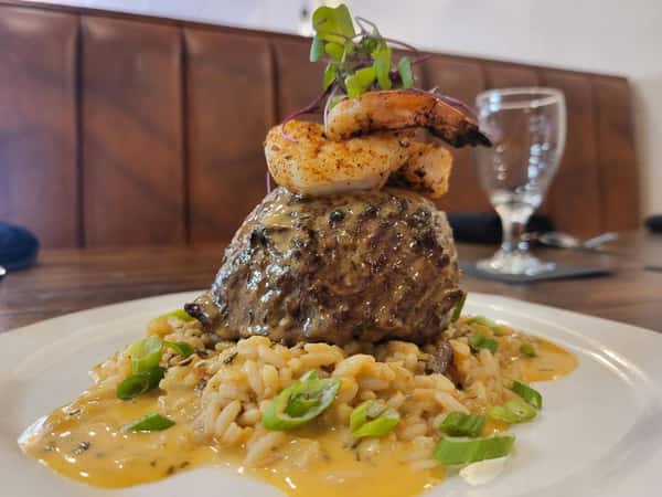 Grilled filet topped with shrimp and microgreens, served over creamy risotto with a savory sauce and garnished with green onions.