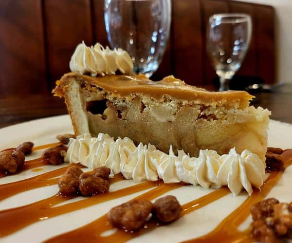 Slice of gooey butter cake topped with whipped cream, caramel drizzle, and candied pecans on a white plate.