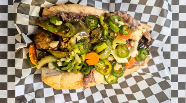 Italian beef sandwich with chopped giardiniera, jalapeños, and beef on a white bun, wrapped in checkered paper.