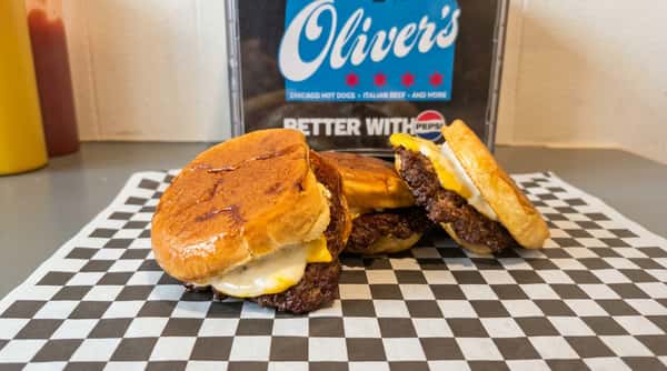 Three mini burgers with beef patties and melted cheese on toasted buns, on checkered paper.