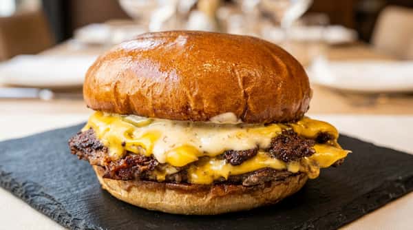 Cheeseburger with a shiny brown bun, melted orange and white cheese, and a beef patty, on a dark surface.