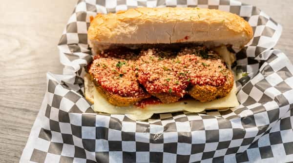 Meatball sub with mozzarella cheese, tomato sauce, parmesan, and herbs served in checkered paper.