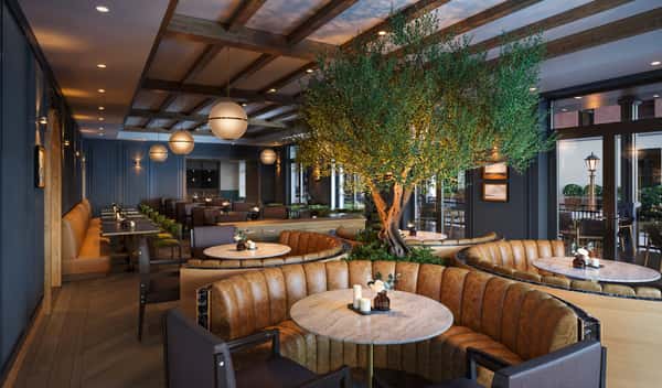 Elegant restaurant interior featuring circular leather booths, round marble tables, and a large illuminated tree as the centerpiece.