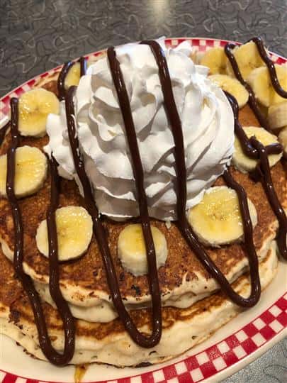 Two pancakes with bananas, whipped cream, and chocolate syrup on top