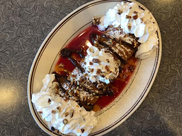 a crepe covered in whipped cream, strawberry sauce, and chocolate drizzle on a plate