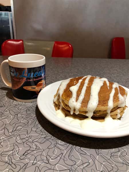 two buttermilk pancakes on a plate drizzled in gravy with a coffee mug next to it