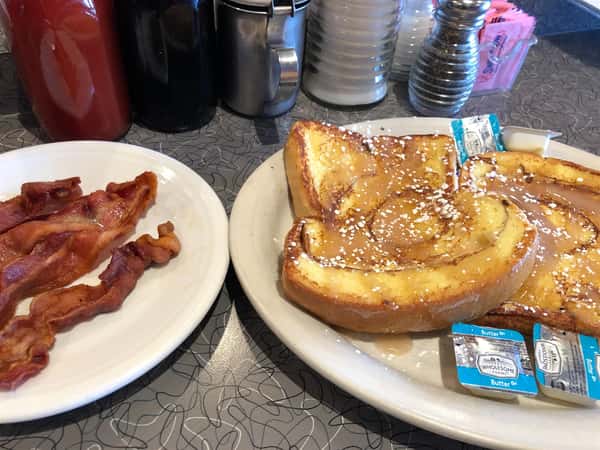 two slices of french toast on a plate next to a plate of a couple of slices of bacon