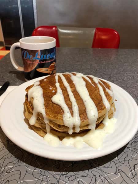 two buttermilk pancakes on a plate drizzled in gravy with a coffee mug next to it