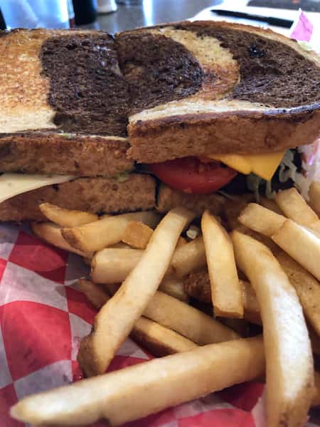 a cheeseburger with lettuce and tomato on marble rye with a side of fries